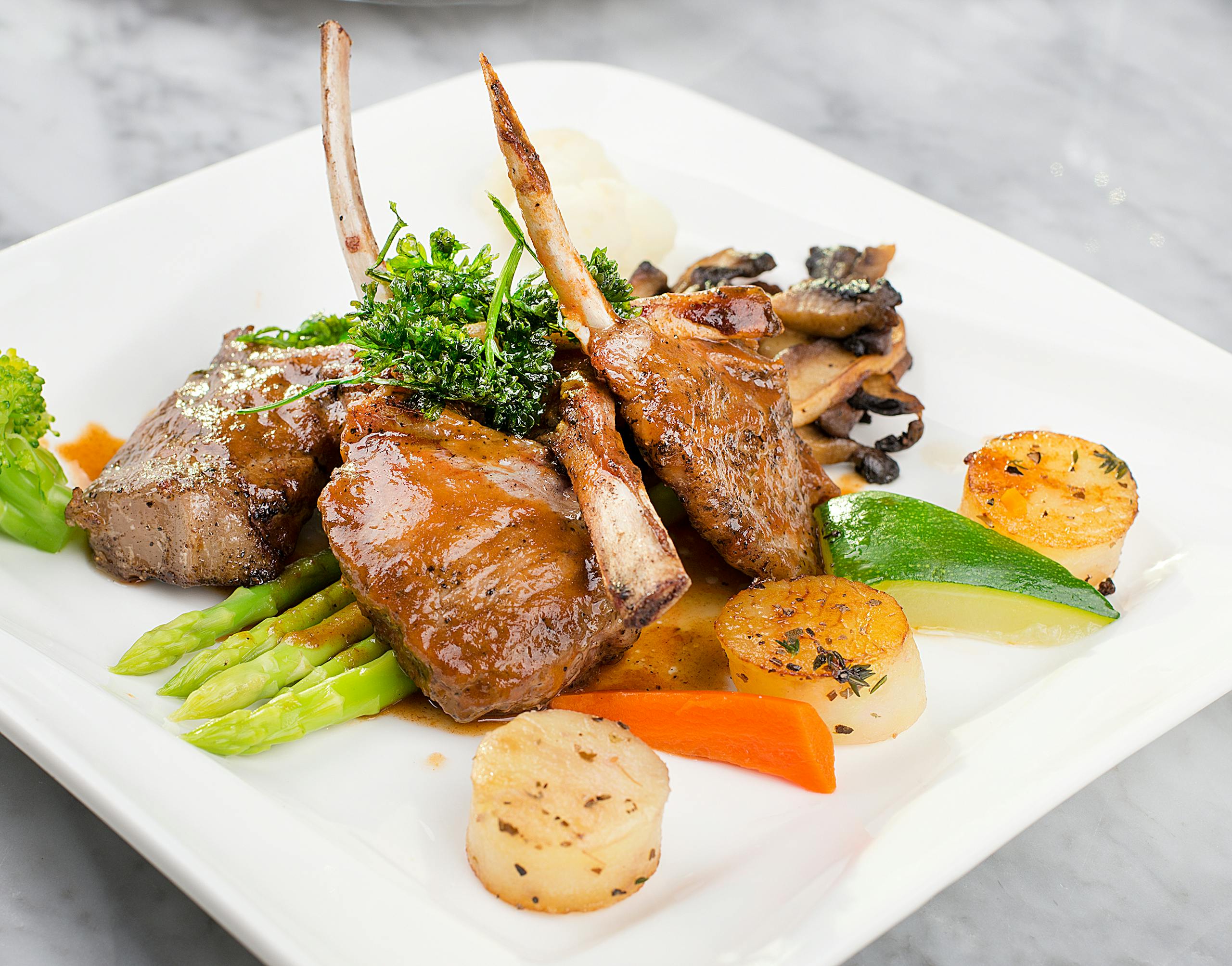 Delicious lamb chops with vegetables plated elegantly on a marble surface.