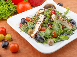 Delicious Mediterranean salad with grilled cheese, olives, and cherry tomatoes on a plate.