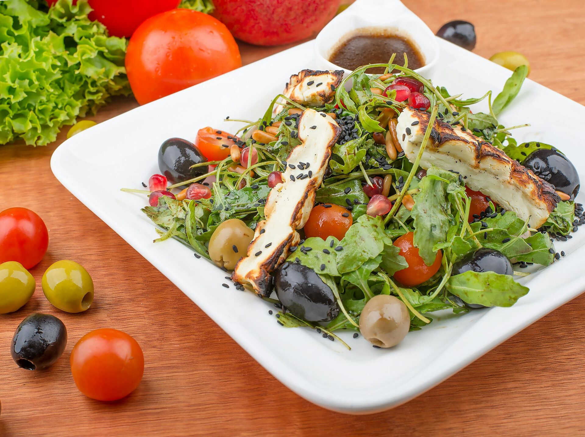 Delicious Mediterranean salad with grilled cheese, olives, and cherry tomatoes on a plate.