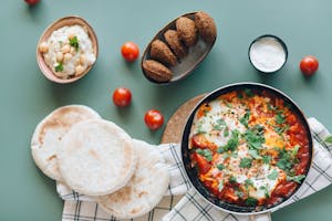 Delicious Middle Eastern breakfast with shakshuka, falafel, hummus, and pita bread on a table.