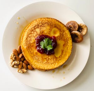 Delicious pancake topped with berry jam, surrounded by almonds and figs, perfect for brunch.