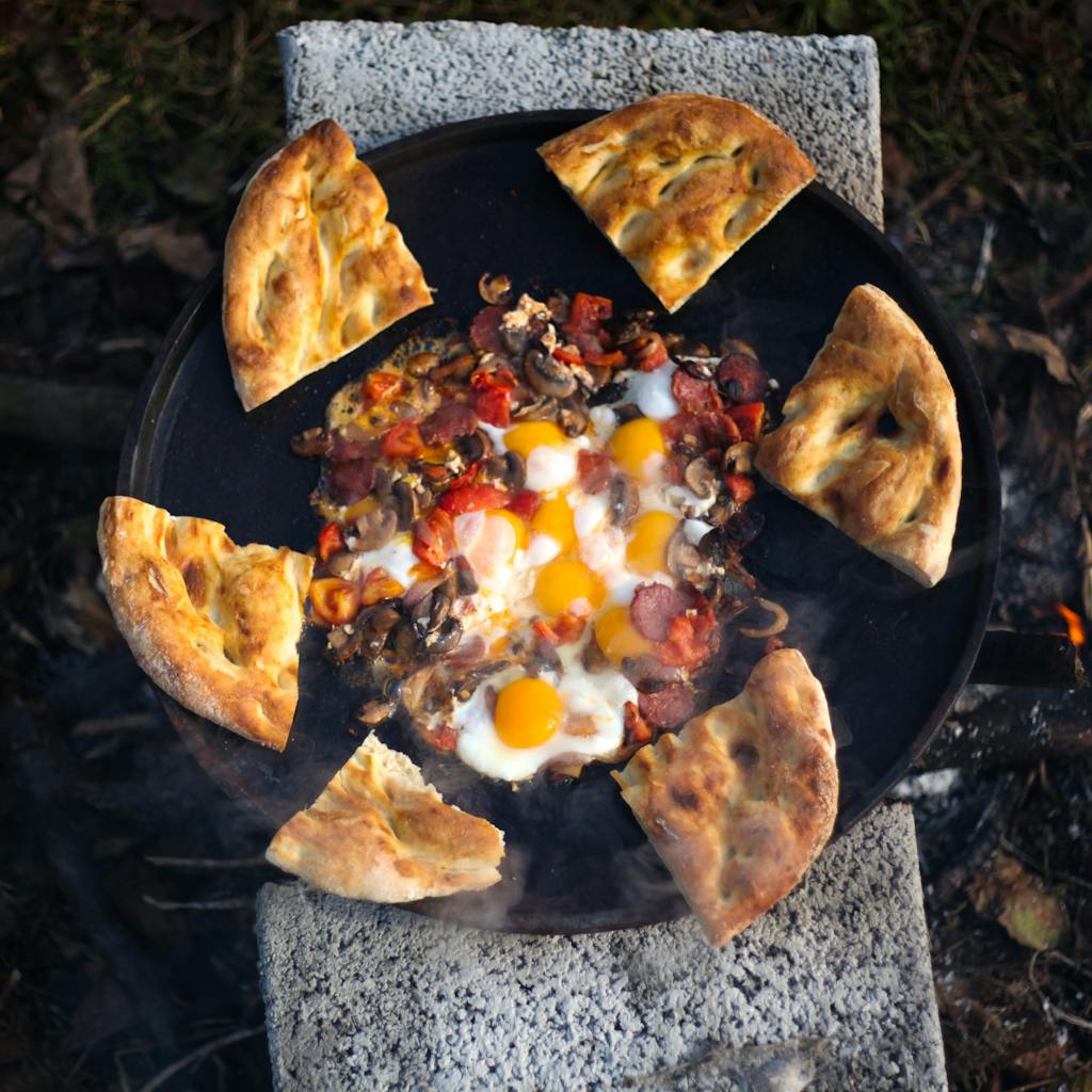 Delicious pizza topped with eggs and mushrooms cooked outdoors over open flame.