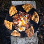 Delicious pizza topped with eggs and mushrooms cooked outdoors over open flame.