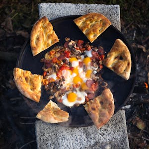 Delicious pizza topped with eggs and mushrooms cooked outdoors over open flame.