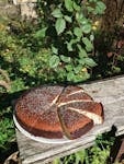 Delicious rustic cake with seeds, sliced and placed on a wooden bench outdoors in daylight.