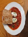 Delicious shakshuka with poached eggs and crusty bread on a decorative plate.