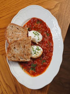 Delicious shakshuka with poached eggs and crusty bread on a decorative plate.