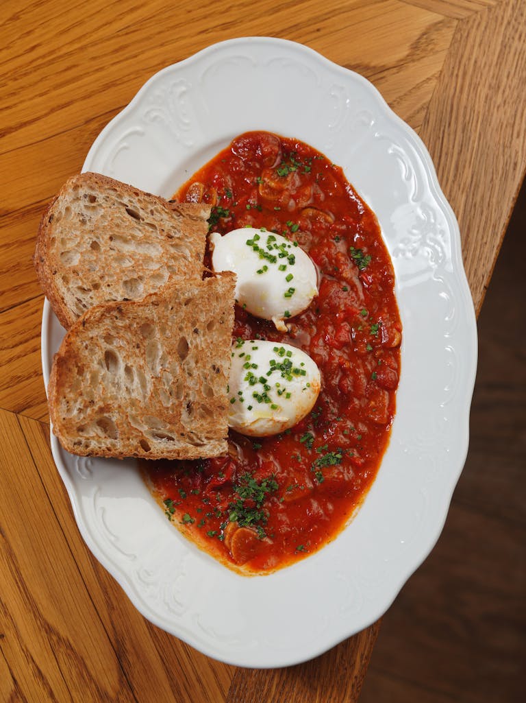 Delicious shakshuka with poached eggs and crusty bread on a decorative plate.