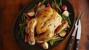 Roasted whole chicken on a platter with green beans, baby carrots, and potatoes.