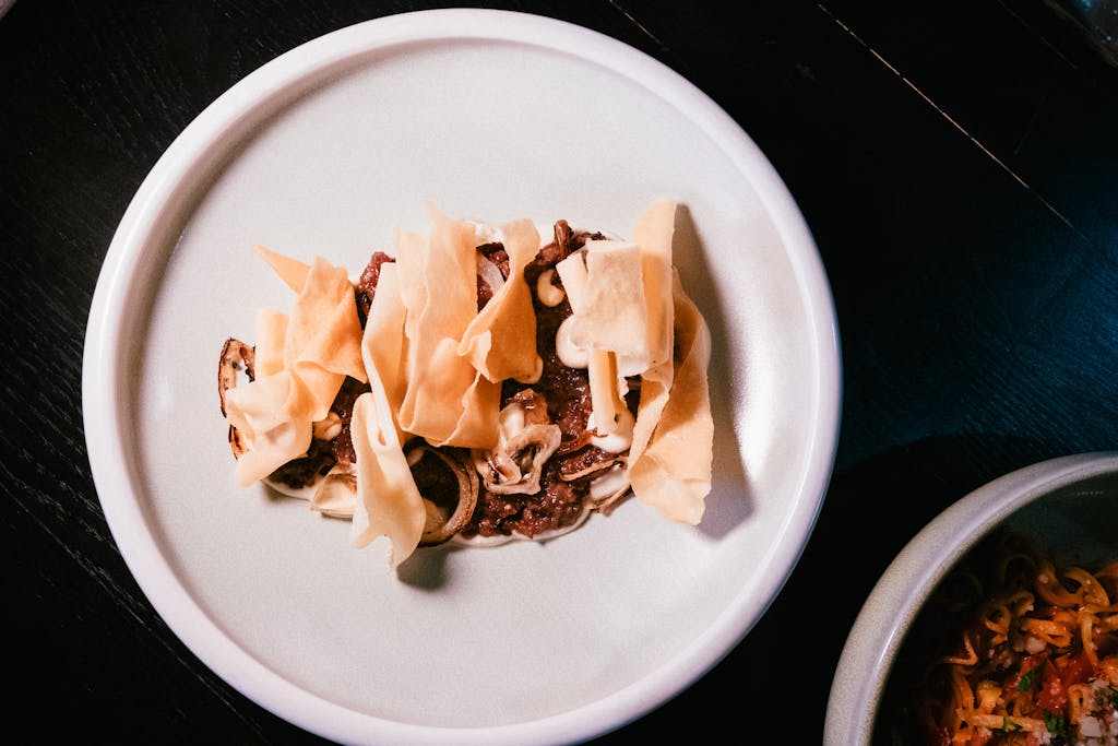 Elegant gourmet dish features crispy wonton chips and savory beef on a ceramic plate.