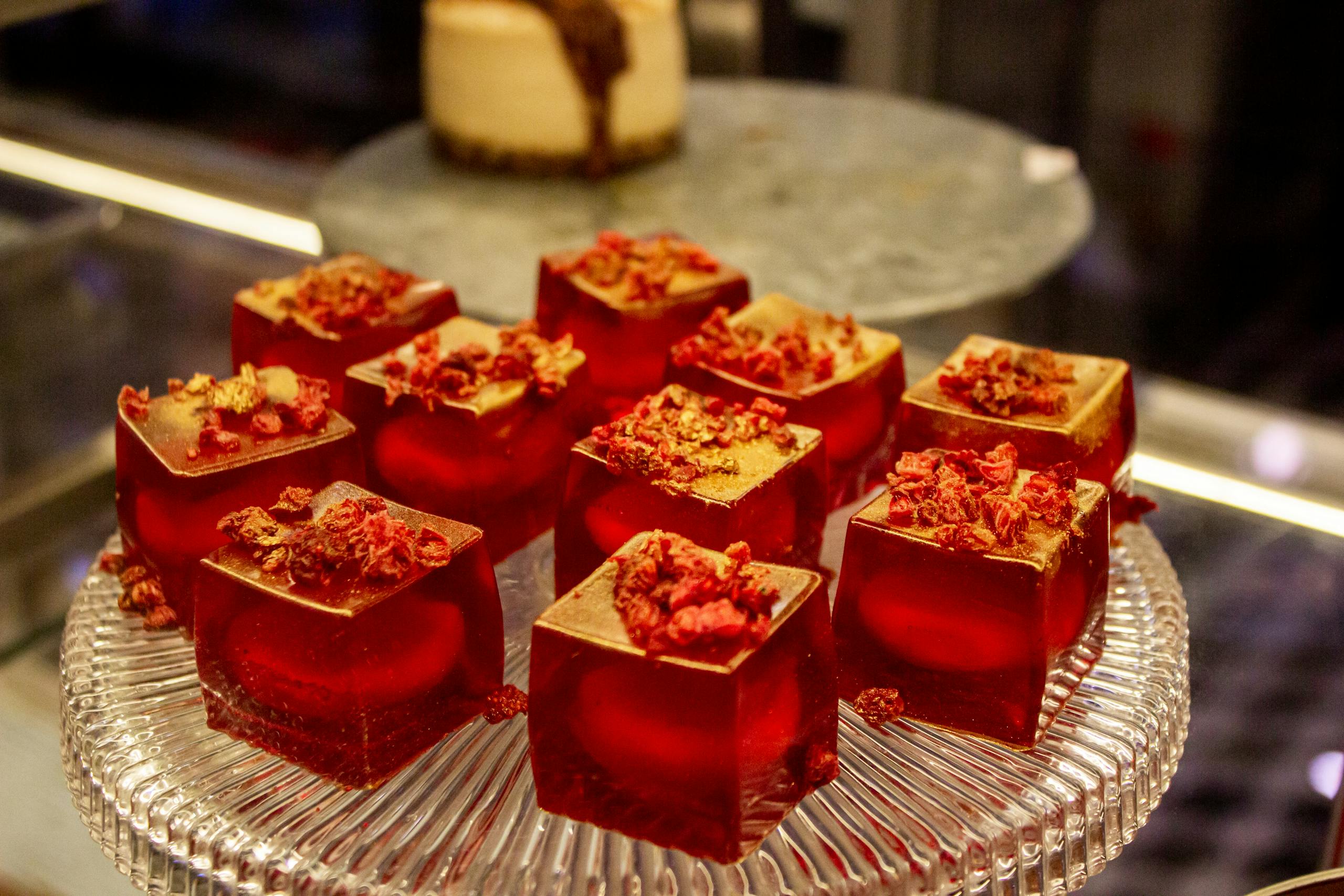 Elegant red jelly desserts topped with gold flakes and berries on a glass platter, perfect for gourmet presentations.