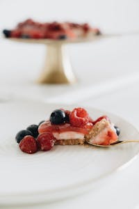 Elegantly plated slice of cheesecake topped with fresh raspberries and blueberries.