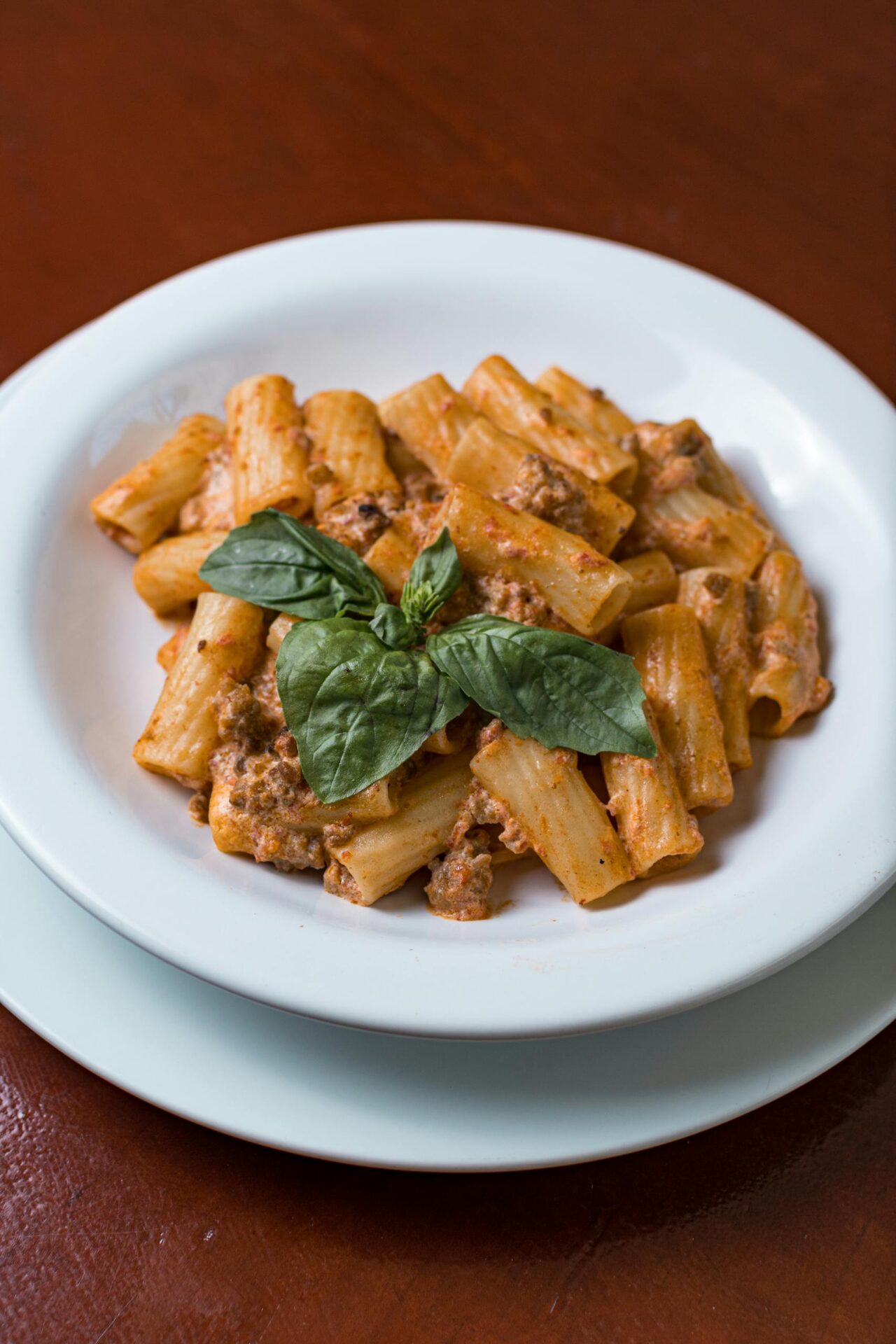 Enjoy a plate of Italian tortiglioni pasta with a rich tomato and meat sauce, garnished with fresh basil.