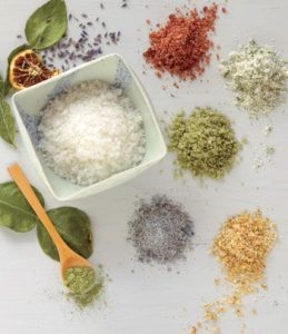 Bowl of coarse salt surrounded by several colored flavored salt blends.
