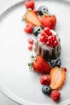 From above of appetizing pie decorated with redcurrant served on white plate with sprinkled sugar and arranged berries with blurred background