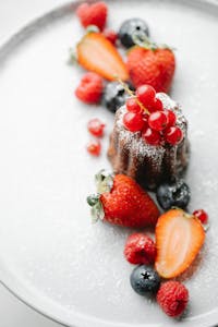 From above of appetizing pie decorated with redcurrant served on white plate with sprinkled sugar and arranged berries with blurred background