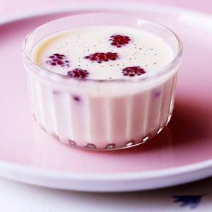 Panna cotta in a glass cup topped with berries on a pink plate.