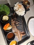 Grilled beef served with rice, pickles, and sauce on a stylish plate.