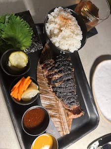 Grilled beef served with rice, pickles, and sauce on a stylish plate.