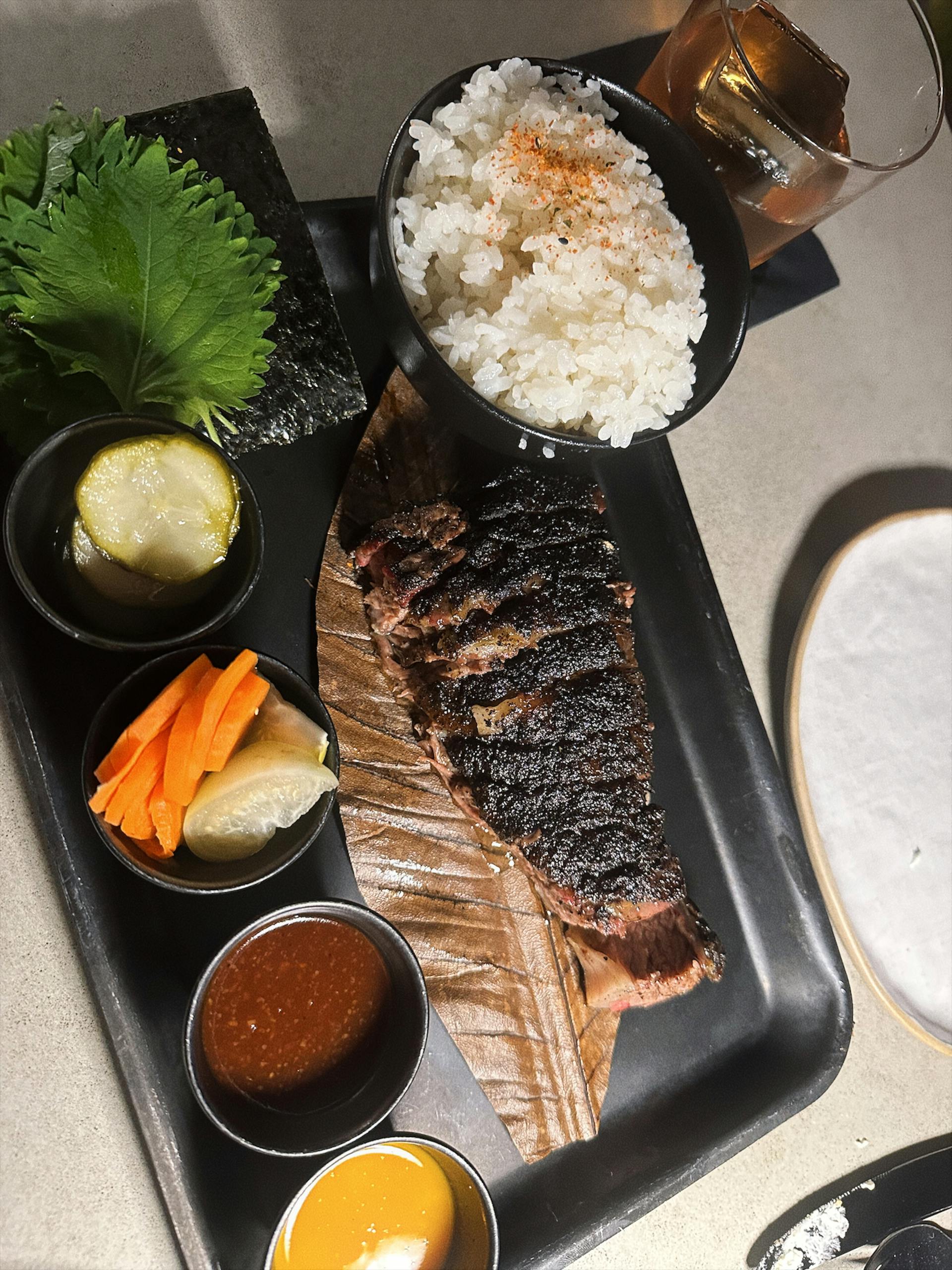Grilled beef served with rice, pickles, and sauce on a stylish plate.