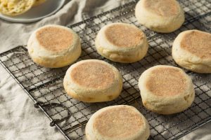 Toasted English muffins on a cooling rack with butter on a plate nearby.