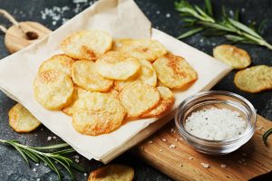Homemade potato chips with sea salt and rosemary on a wooden cutting board