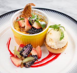 Indulge in a gourmet crème brûlée topped with blackberries and strawberries, paired with vanilla ice cream.