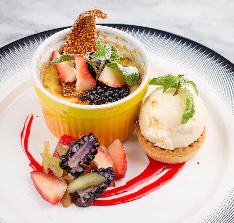 Indulge in a gourmet crème brûlée topped with blackberries and strawberries, paired with vanilla ice cream.