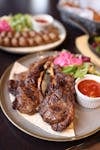 Juicy grilled lamb chops served with fresh salad and spicy sauce on a rustic plate.