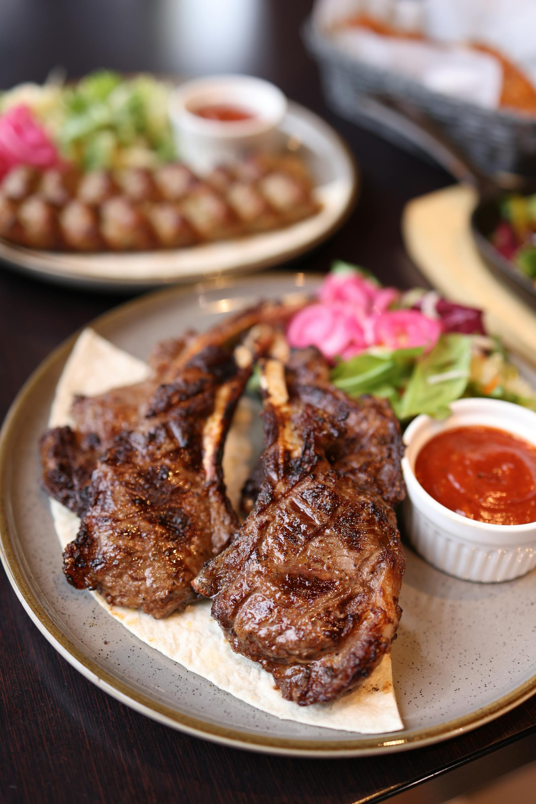 Juicy grilled lamb chops served with fresh salad and spicy sauce on a rustic plate.