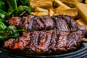 Juicy grilled steak with roasted green peppers and crispy potatoes for a savory meal.