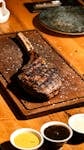 Juicy grilled tomahawk steak on a wooden board with three dipping sauces.
