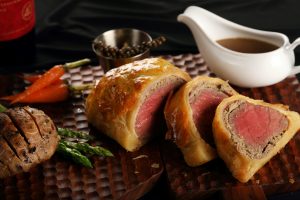 Sliced Beef Wellington with gravy, carrots, and asparagus.