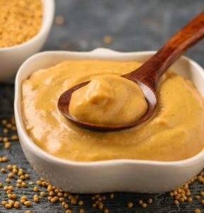 Bowl of smooth homemade mustard with a wooden spoon.
