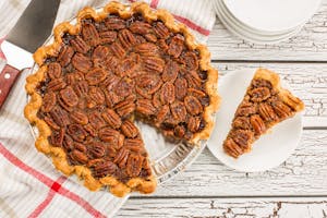 Overhead view of a pecan pie with a slice removed, set on a rustic white table.