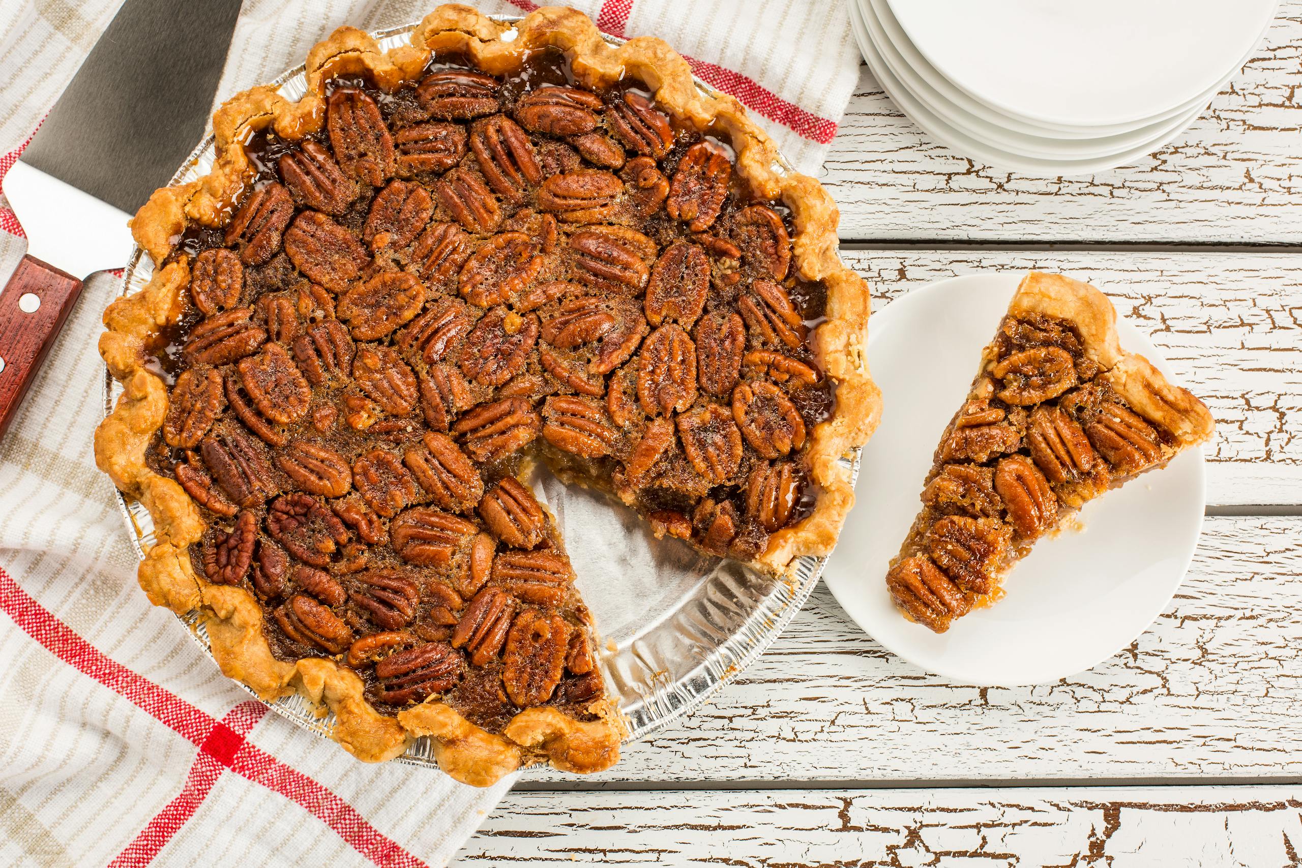 Overhead view of a pecan pie with a slice removed, set on a rustic white table.