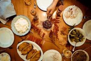 Overhead view of a traditional Thanksgiving dinner table with various dishes and autumn leaves.