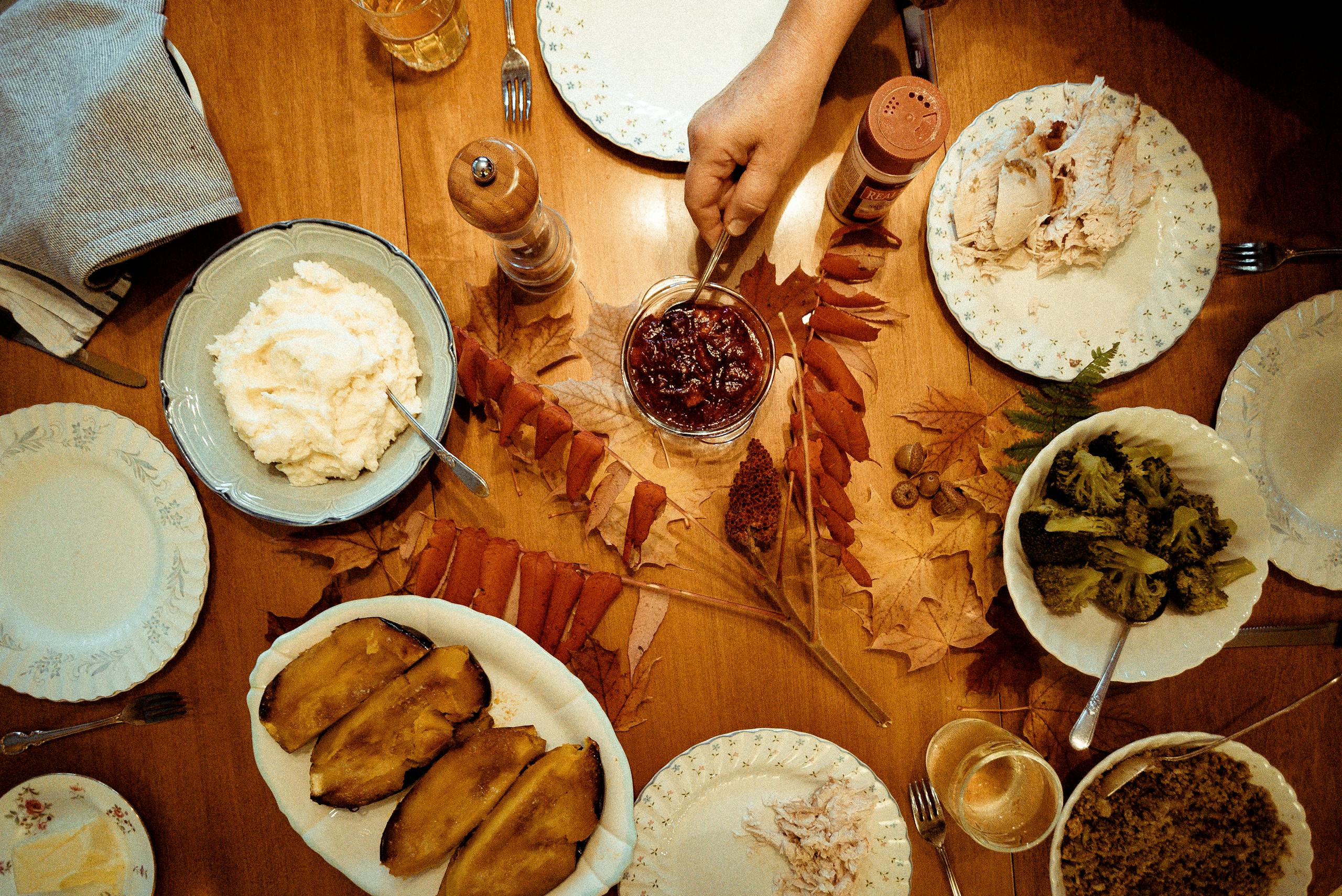 Overhead view of a traditional Thanksgiving dinner table with various dishes and autumn leaves.