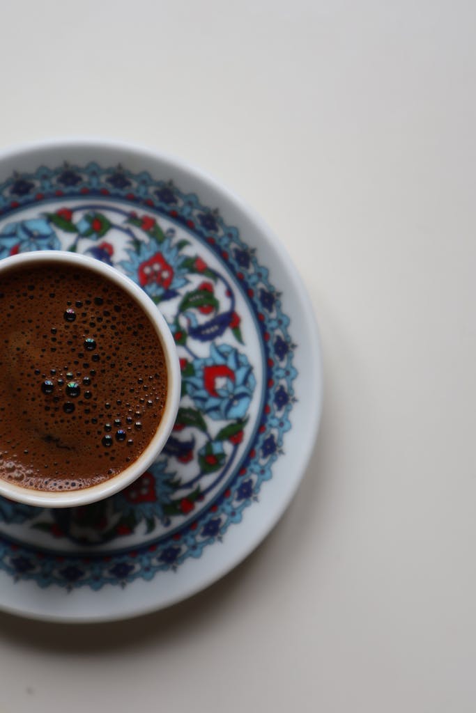 Overhead view of Turkish coffee in a colorful floral cup and saucer on white background.