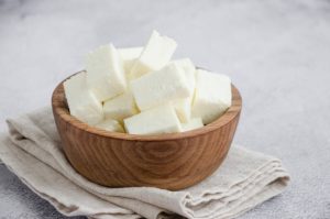 Paneer cubes in a wooden bowl on folded cloth.