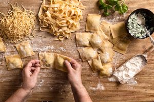Hands shaping fresh pasta on a floured wooden surface.