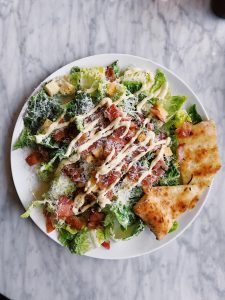 Caesar salad with bacon, croutons, grated cheese, and dressing on a white plate.