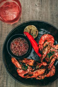 Grilled shrimp with dipping sauce, lime, and red pepper on a dark plate