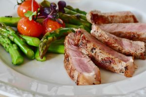 Sliced pork tenderloin with asparagus and cherry tomatoes on a white plate.