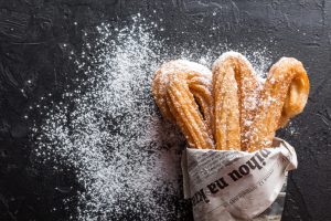 Churros dusted with powdered sugar in a paper wrap.