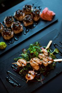 Shrimp skewers over mixed greens with balsamic glaze on black plates.