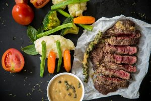 Sliced peppercorn-crusted steak with mixed vegetables, mashed potatoes, and peppercorn sauce