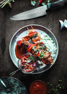 Grilled chicken skewers with vegetables, rice, and salsa on a plate