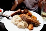 Plate of roast pork ribs, sauerkraut, and potatoes served in a cozy setting.