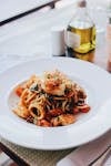 Plate of spaghetti with shrimp and calamari garnished with herbs, captured indoors.